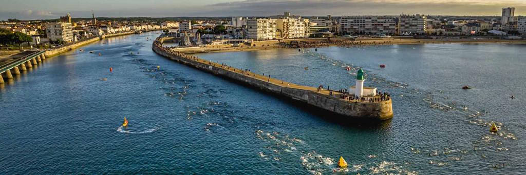 View of the Atlantic Ocean and athletes running on the promenade along the Tanchet lake at IRONMAN 70.3 Les Sables d'Olonne