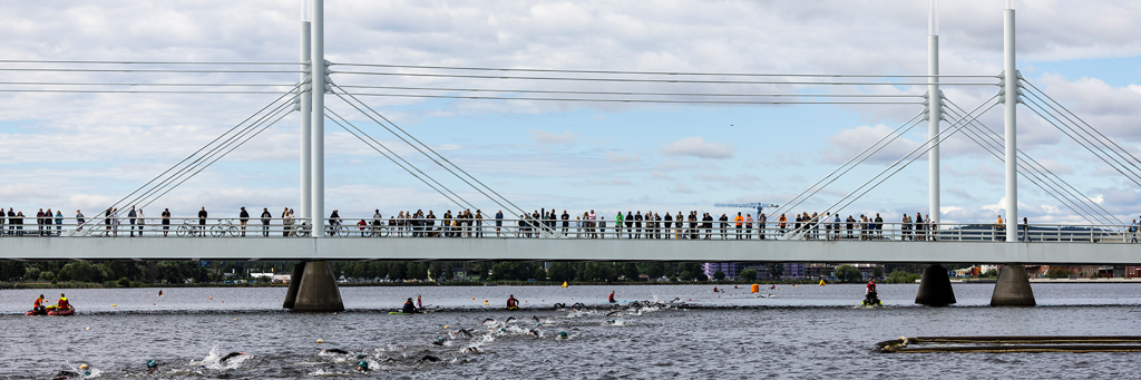 Supporters standing on a bridge and watching athletes swimming at IRONMAN 70.3 Jönköping