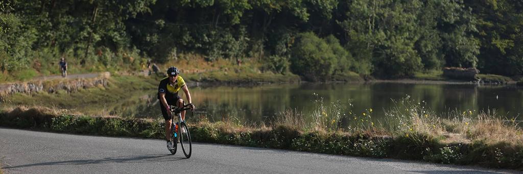 IRONMAN Ireland Cork athletes biking on a lane surrounded by trees and fields on a rainy day
