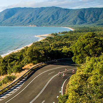 Triathletes biking along scenic view near water at IM703 Cairns