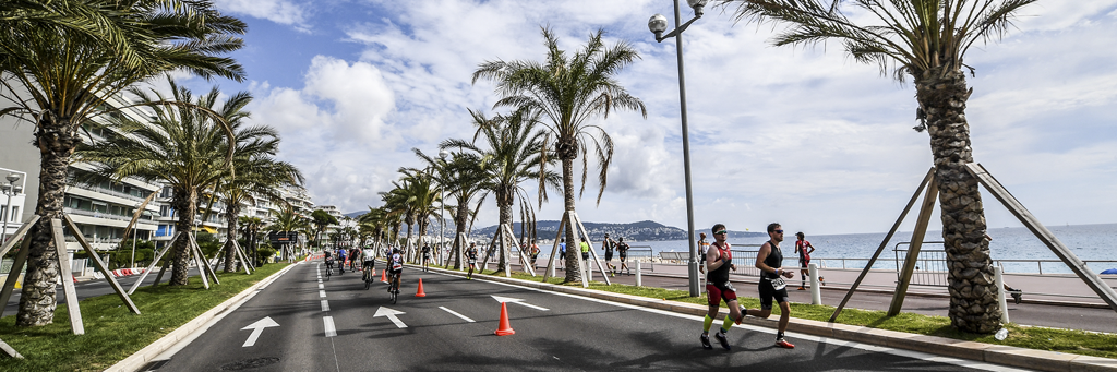 Athletes are running on the Promenade de Anglais along an avenue of palm trees and next to the beach at IRONMAN 70.3 Nice