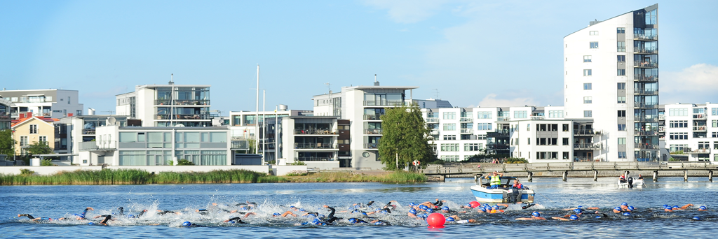 Athletes with blue swim caps are swimming at Kattrumpan beach at Kalmar Mini Tri next to houses on the shore
