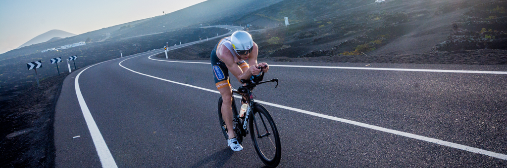 An IRONMAN 70.3 Lanzarote athlete biking at a winding street in the stark landscape of the southern part of the island
