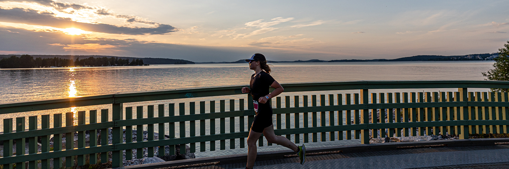 Female athlete running over a bridge next to a lake in Finland at sundown at IRONMAN 70.3 Lahti