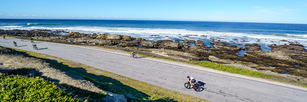 Athletes biking on the rugged coastline next to the turquoise sea and foaming waves