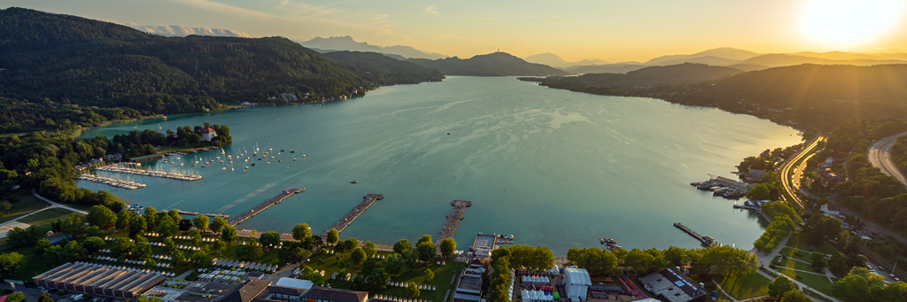 Bird's eye view of Lake Wörth and several cities in Carinthia at sunset with Pyramidenkogel in the background