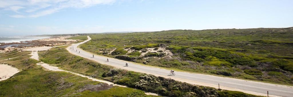 Athletes biking on the rugged coastline next to the turquoise sea and foaming waves