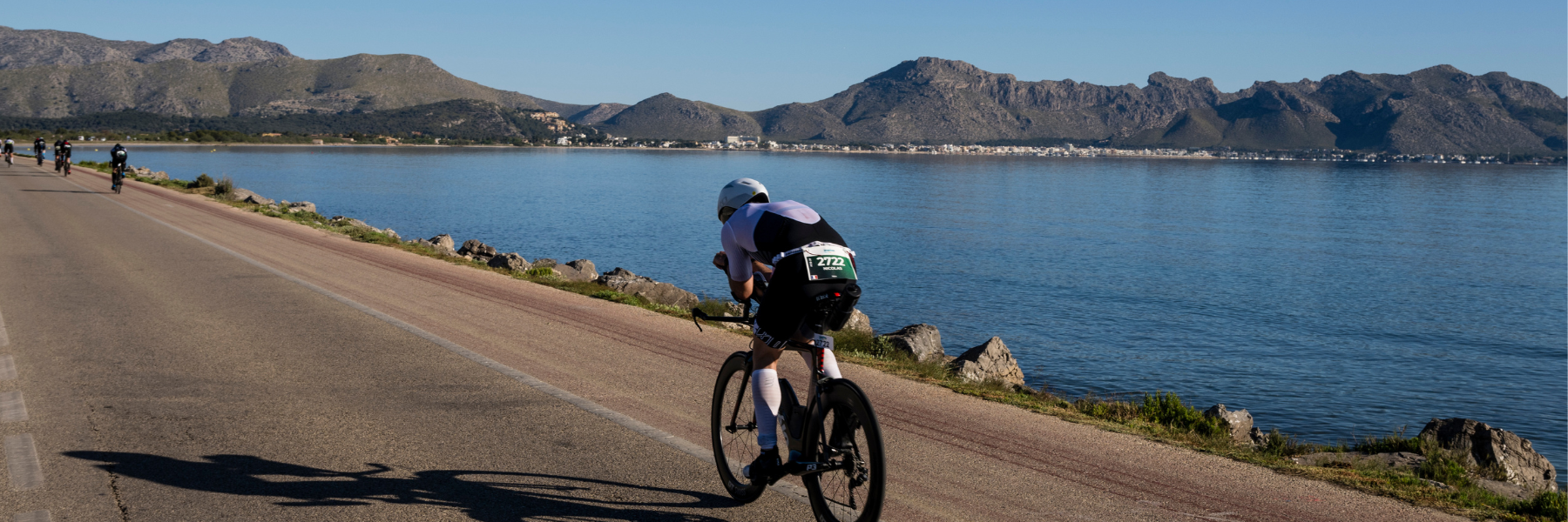 A single athlete who is biking along a street next to the sea on a cloud free and sunny day at IRONMAN 70.3 Mallorca