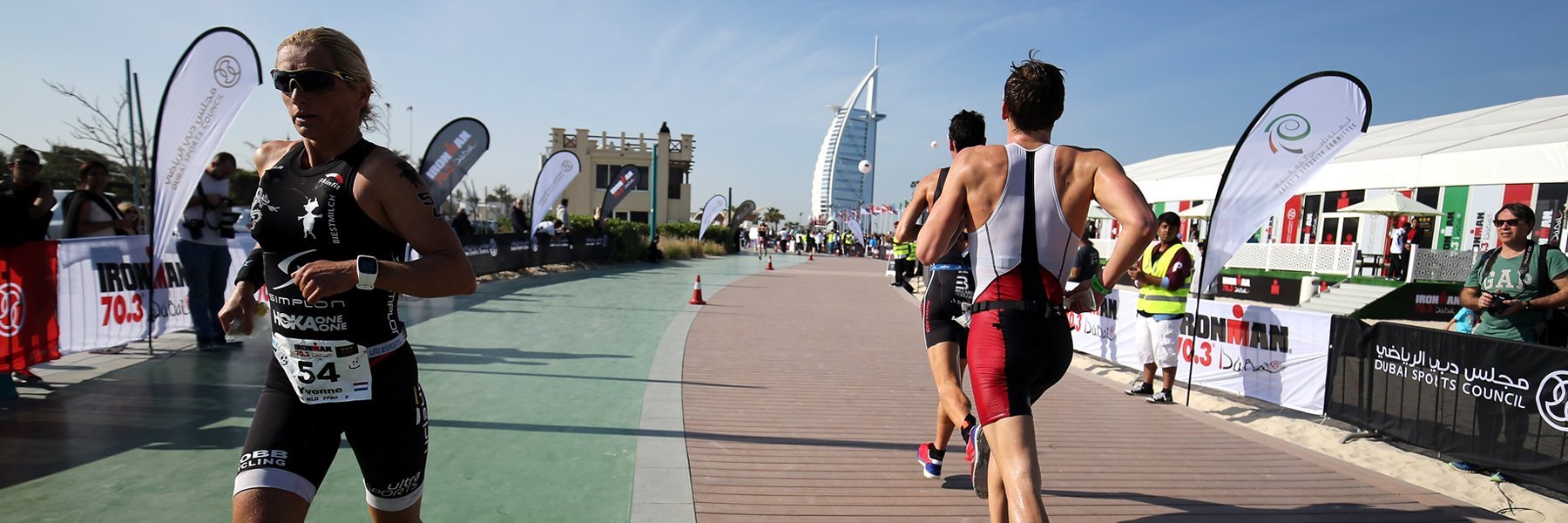Athletes are running at Jumeirah Public Beach along the coastline with spectators on both sides cheering them on at IRONMAN 70.3 Dubai