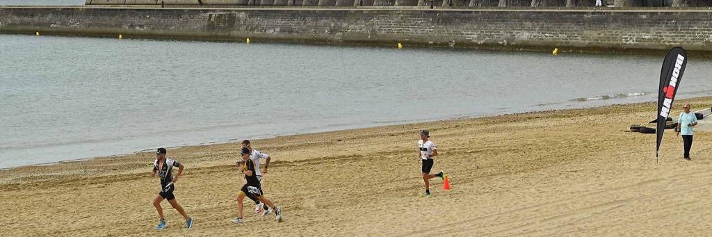 IRONMAN 70.3 Les Sables d'Olonne athletes swimming towards historic Vendée Globe canal next to a pier with a lighthouse