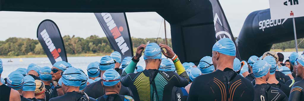 Athletes with blue swim caps standing next to each other and waiting to take on the swim course in lake Harku at IRONMAN 70.3 Tallinn
