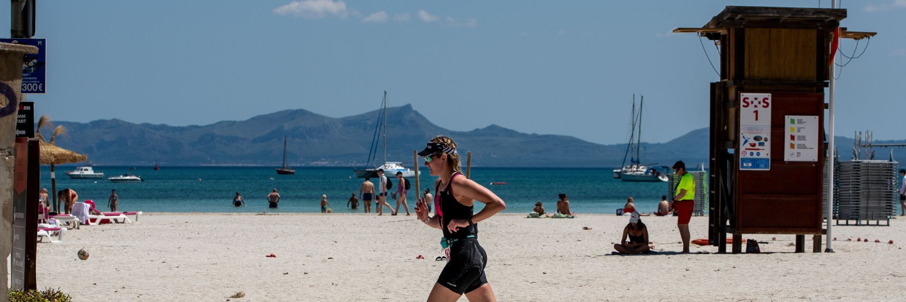 An IRONMAN 70.3 Mallorca athlete running on the flat course along the white beach of Alcúdia Bay