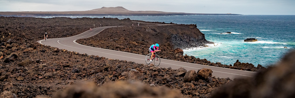 Athletes biking on a street surrounded by black and stark landscape and stunning turquoise sea