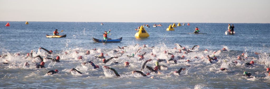 IRONMAN 70.3 Turkey athletes swimming in the crystal-clear water of Turkish Riviera while volunteers in canoes are watching them