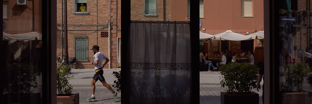 Athlete is running through the heart of Cervia seen through a store at IRONMAN 70.3 Italy Emilia-Romagna