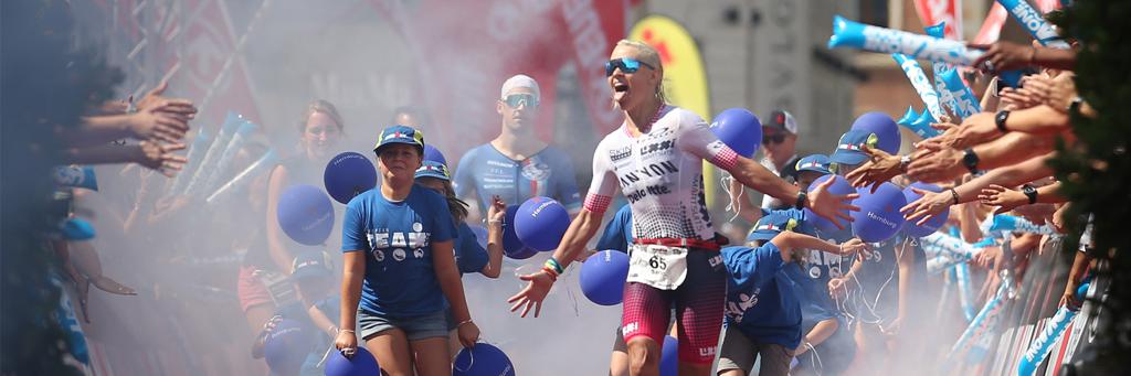 Female athlete is entering the finish line and gets greeted by supporters at IRONMAN Hamburg