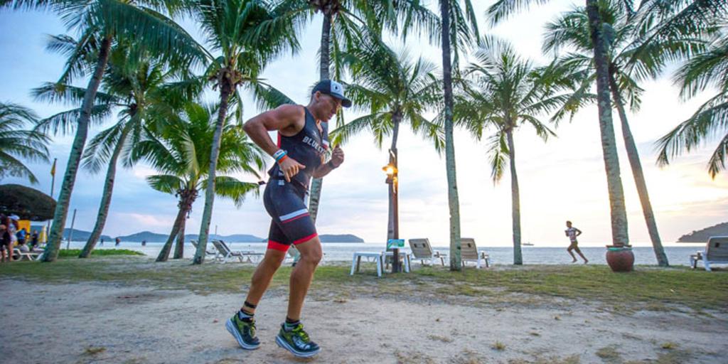 Triathlete running near palm trees and water at IM Malaysia 