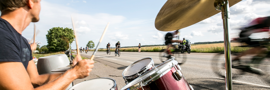 Athletes biking along the street at IRONMAN Kalmar where they are greeted by a music band 