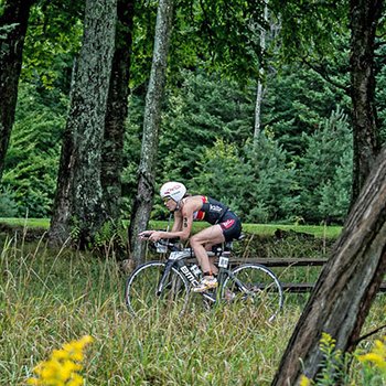 Triathlete biking in wooded area at IM703 Mont Tremblant