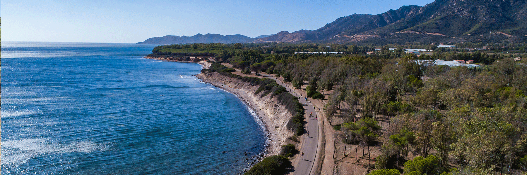 Athletes running on a street on the shore with turquoise Mediterranean Sea on the left and mountains and forests on the right in Santa Margherita di Pula, Sardegna