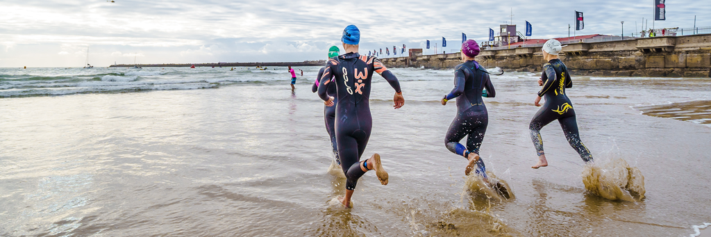 IRONMAN 70.3 South Africa athletes running into the Indian Ocean at Orient Beach next to a pier in East London, Buffalo City