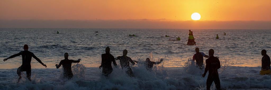 Close-up from below of IRONMAN African Championship athletes running into the sea at Hobie Beach at sunrise