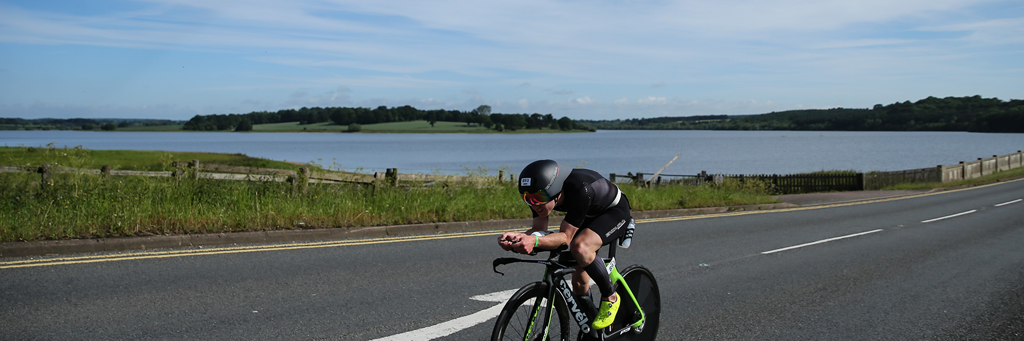 A single IRONMAN 70.3 Staffordshire athlete biking through the heart of the Staffordshire countryside crossing a bridge over Blithfield Reservoir