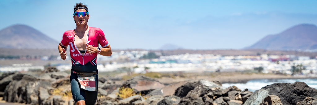 IRONMAN Lanzarote athlete running along Avenida de Las Playas during intense sunshine and beautiful views in the background