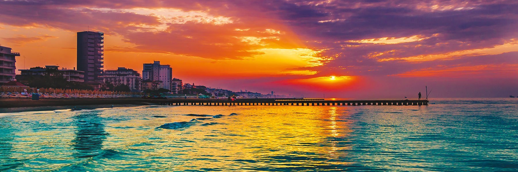 People on a pier on the beach in Jesolo at sunset, the colors the sky red and is reflected in the Mediterranean Sea