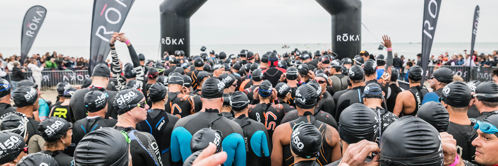 Overview of 5150 Cervia athletes with black swim caps under the start arch ready to take on the swim in the Adriatic Sea