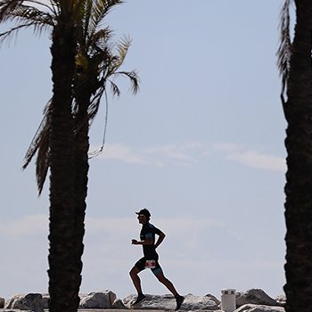 IRONMAN 70.3 Marbella athlete running along the beach next to palm trees