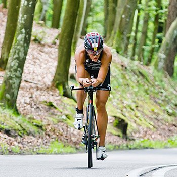 A single athlete on his bike on the street in the middle of the woods at Enea IRONMAN 70.3 Gdynia