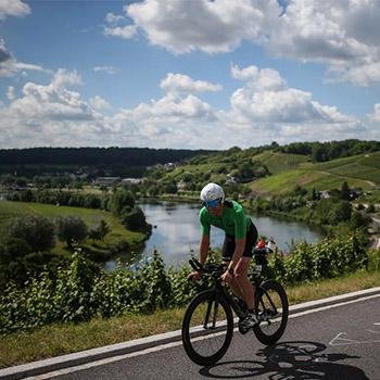 Athlete biking between riverside and the scenic vineyards at IRONMAN 70.3 Luxembourg-Région Moselle