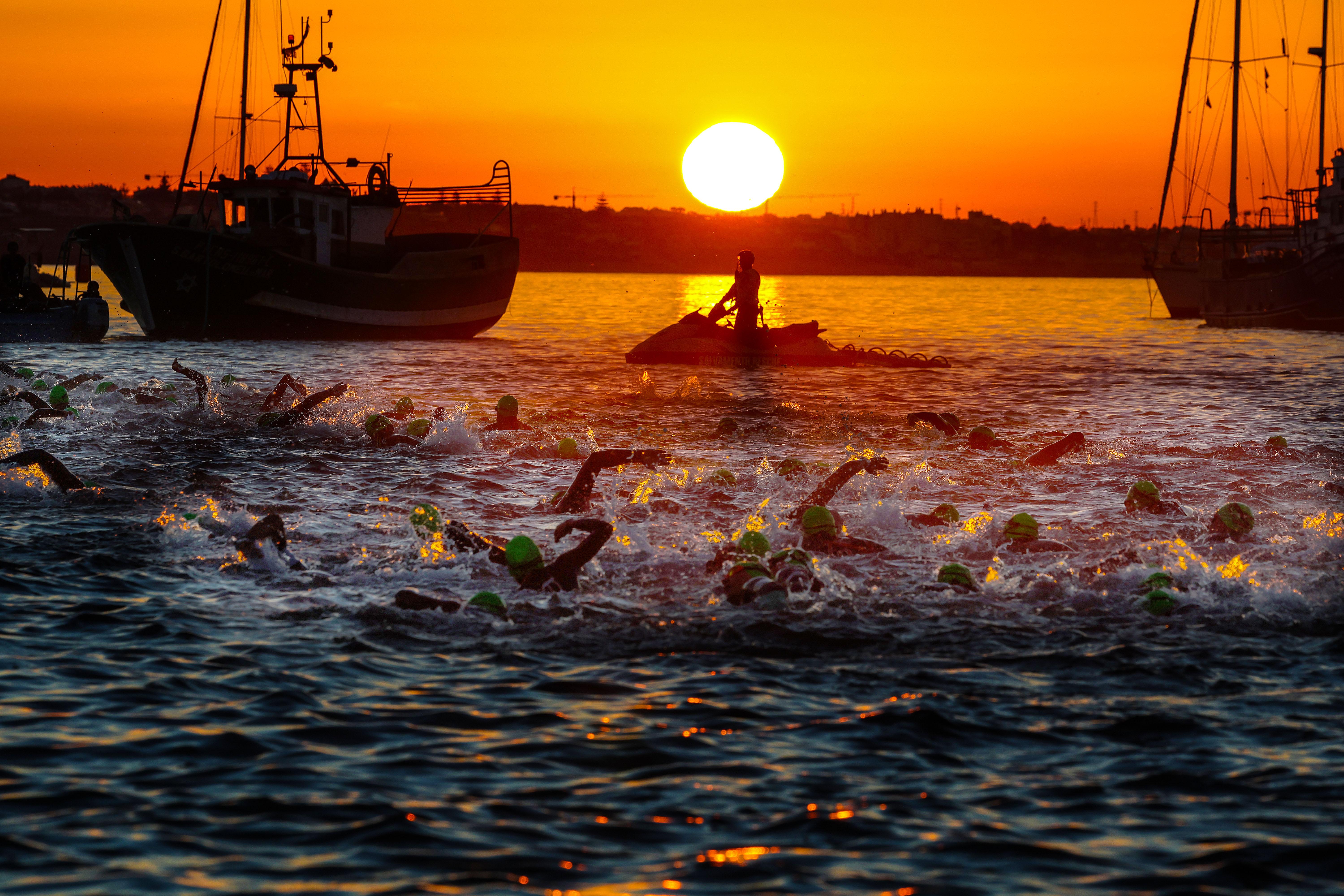 Atletas a nadar na baía de Cascais ao nascer do sol no IRONMAN 70.3 Portugal